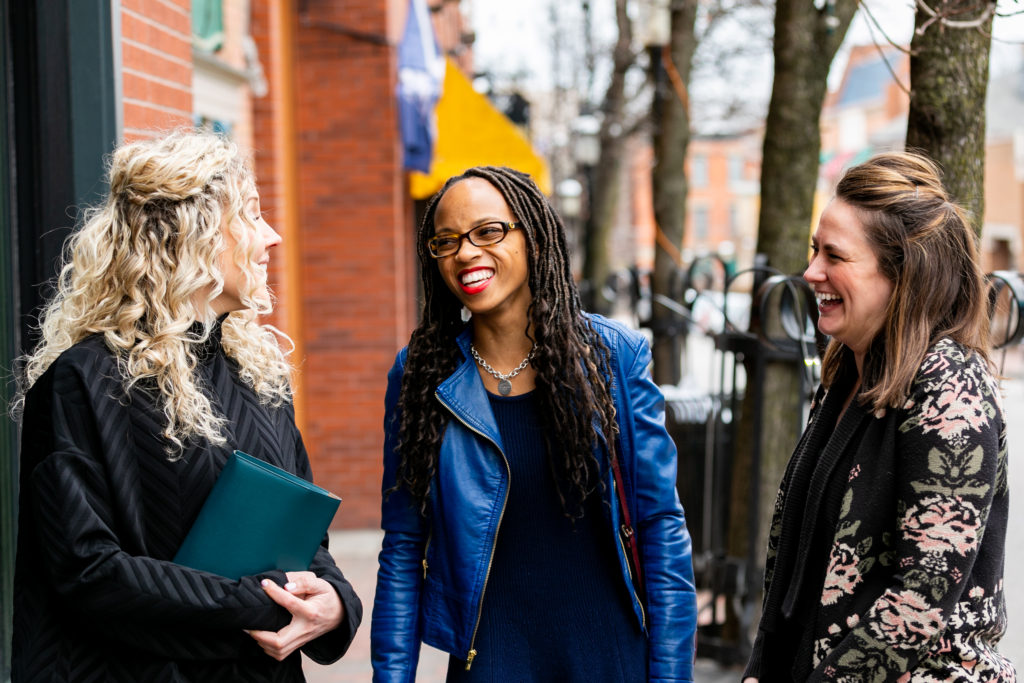 African American woman walking with two Caucasian women on the street, smiling